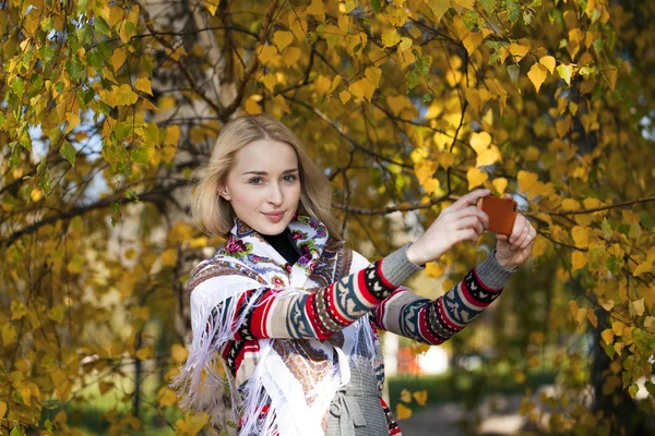 Gelukkig mooi meisje gefotografeerd op een mobiele telefoon in de herfst park — Stockfoto