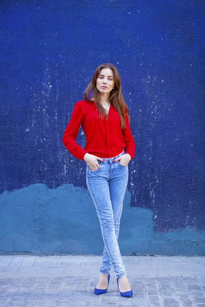 Joven chica hermosa en vaqueros azules y una camisa roja en el backgr — Foto de Stock