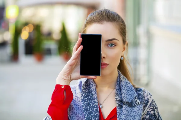 Mladá žena se vztahuje na její tvář obrazovka smartphone — Stock fotografie