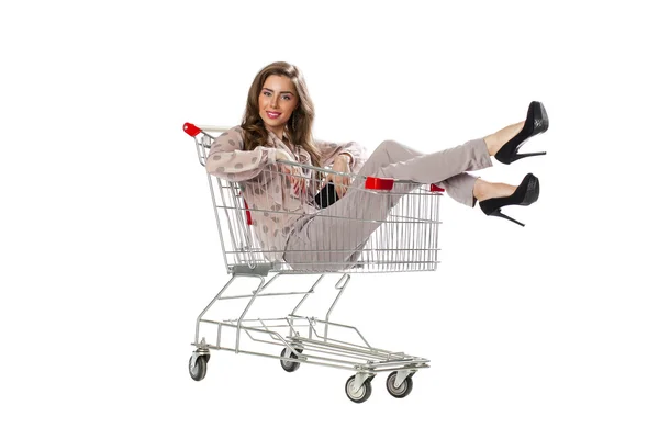 Young beautiful brunette girl sits in an empty shopping cart — Stock fotografie