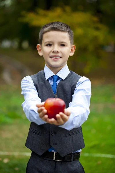 Malý chlapec drží červené jablko na pozadí podzimního parku — Stock fotografie