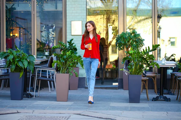 Young beautiful girl in jeans and a red blouse is walking down t — Stock Photo, Image