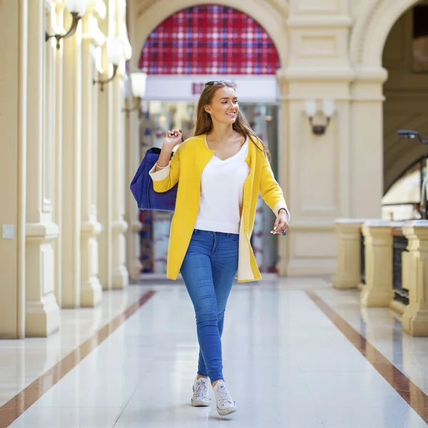 Mujer joven con abrigo amarillo caminando en la tienda —  Fotos de Stock