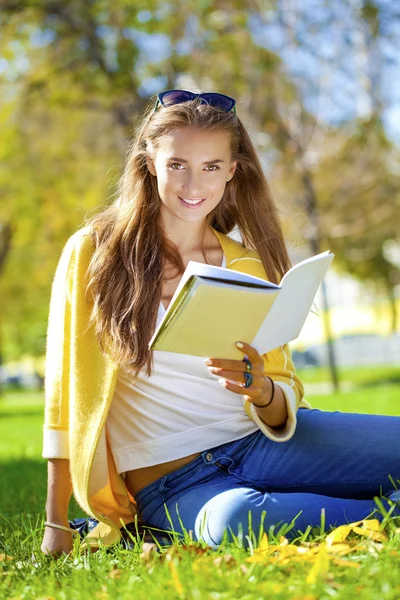 Hermosa estudiante sentada en el parque de otoño y leyendo un libro — Foto de Stock