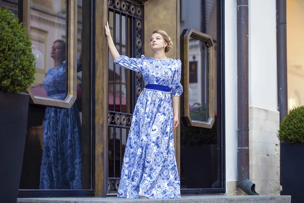 Prachtige blond meisje in blauwe jurk poseren tegen een achtergrond — Stockfoto