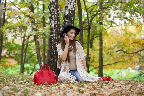 Happy beautiful woman calling by phone sitting in the autumn par — Stock Photo, Image