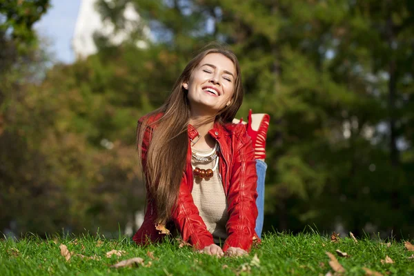 Glücklich schöne Frau in roter Lederjacke sitzt im Herbst — Stockfoto