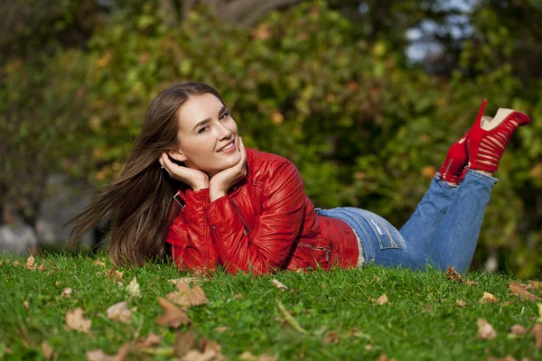 Hppy piękna kobieta w czerwonej skórzanej kurtce i niebieskie dżinsy sittin — Zdjęcie stockowe