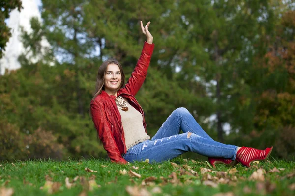 Hppy beautiful woman in red leather jacket and blue jeans sittin — Stock Photo, Image