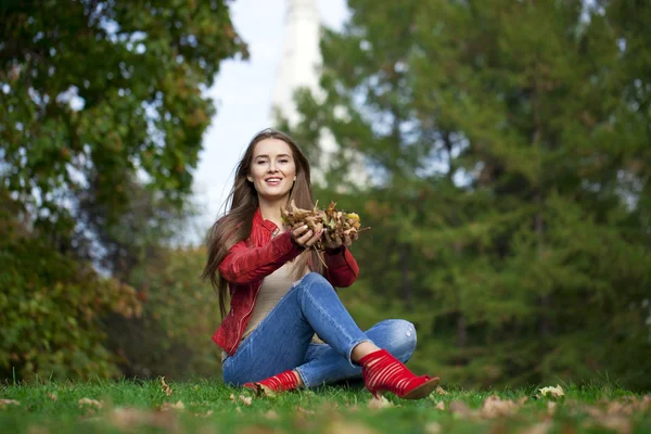 Hppy beautiful woman in red leather jacket and blue jeans sittin — Stock Photo, Image