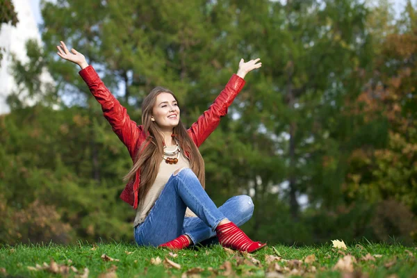 Hppy beautiful woman in red leather jacket and blue jeans sittin — Stock Photo, Image