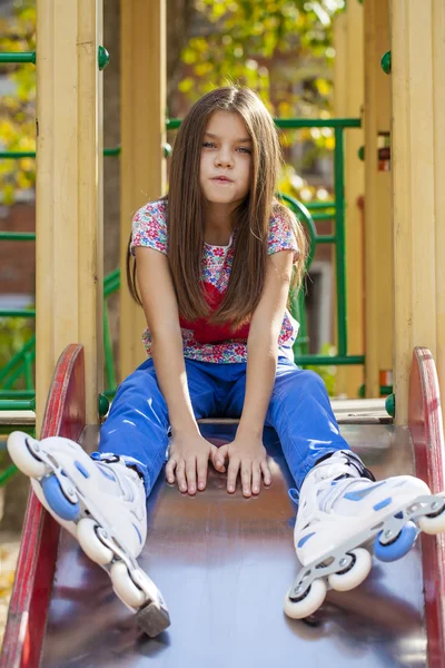 Porträt eines kleinen Mädchens sitzt auf einem Spielplatz in Rollschuhen — Stockfoto