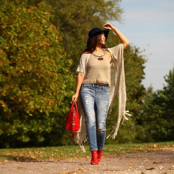 Jeune femme à la mode jeans bleus et sac rouge marchant en automne — Photo