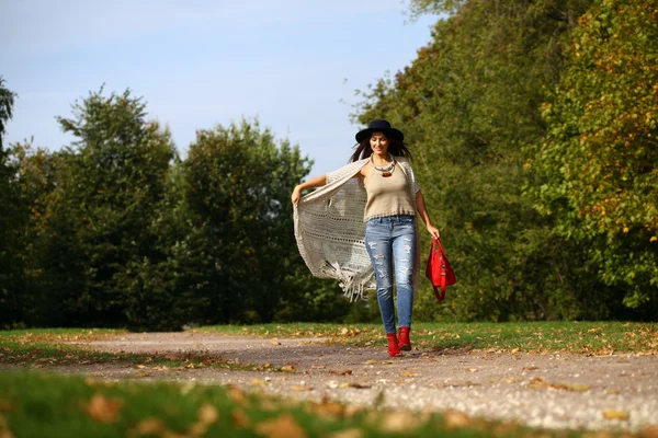 Mujer joven en jeans azules de moda y bolso rojo caminando en otoño —  Fotos de Stock