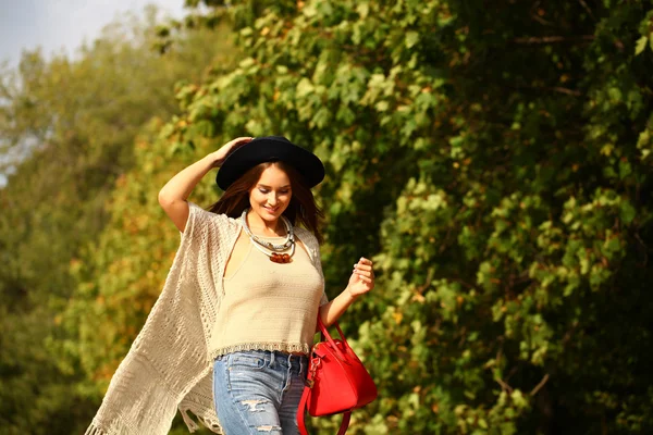 Junge Frau in modischer blauer Jeans und roter Tasche spaziert im Herbst — Stockfoto