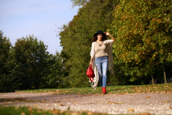 Mujer joven en jeans azules de moda y bolso rojo caminando en otoño —  Fotos de Stock