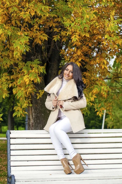 Gyönyörű fiatal barna nő ül egy padon őszén — Stock Fotó