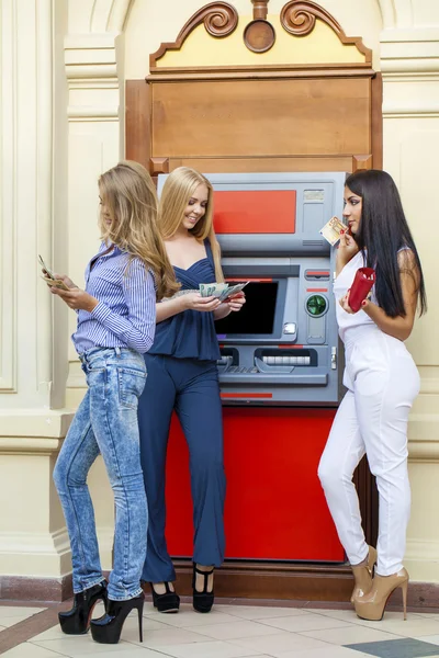Three Young happy women in using an automated teller machine
