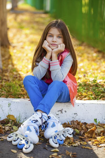 Porträt eines kleinen Mädchens sitzt auf einem Spielplatz in Rollschuhen — Stockfoto