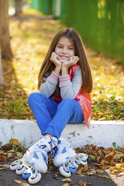 Porträt eines kleinen Mädchens sitzt auf einem Spielplatz in Rollschuhen — Stockfoto