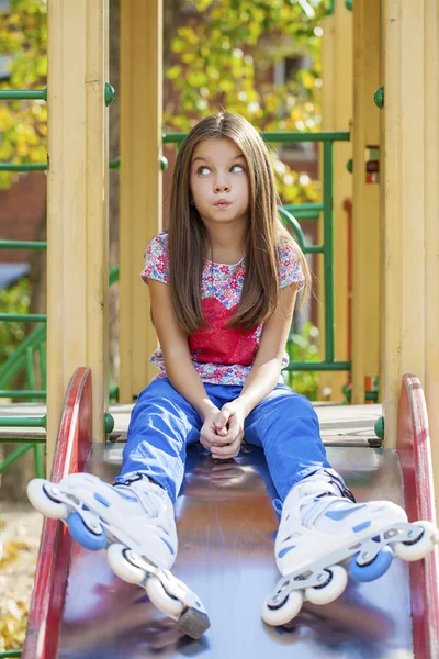 Portret van meisje zit op een speelplaats in rolschaatsen — Stockfoto