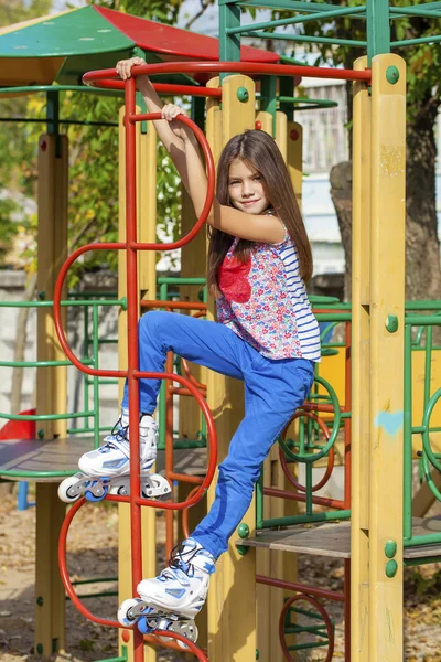 Porträtt av liten flicka sitter på en lekplats i rullskridskor — Stockfoto