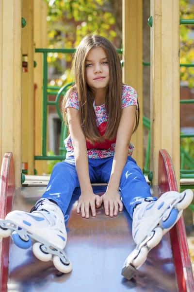 Retrato de menina senta-se em um playground em patins — Fotografia de Stock