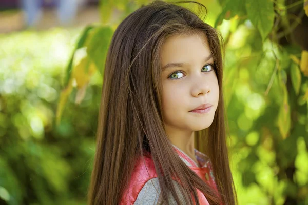 Beautiful little girl on green background of summer city park — Stock Photo, Image