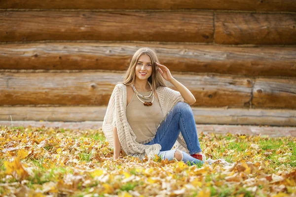 Happy krásná žena v modré džíny sedí v podzimním parku — Stock fotografie