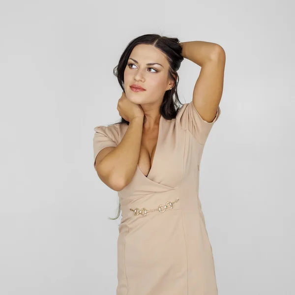 Portret van een mooie sexy brunette in een beige jurk op een grijs — Stockfoto