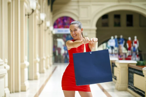 Mooi lachende meisje in een rode jurk, houden van boodschappentassen — Stockfoto