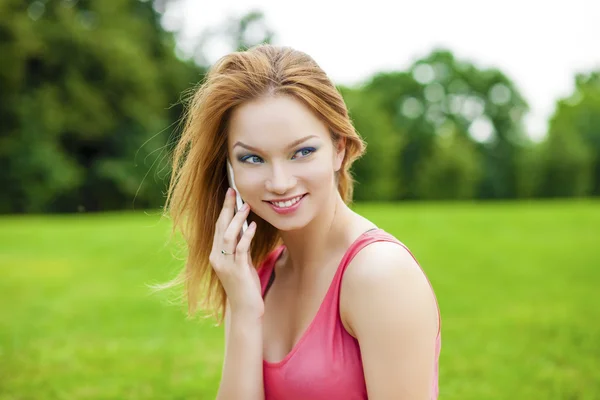 Hermosa mujer joven sonriente pelirroja hablando en un teléfono celular — Foto de Stock