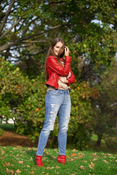 Mujer joven en chaqueta roja de moda y vaqueros azules en el parque de otoño —  Fotos de Stock