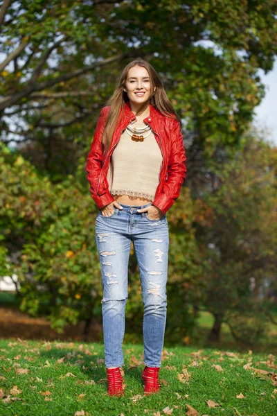 Giovane donna di moda giacca rossa e jeans blu nel parco autunnale — Foto Stock