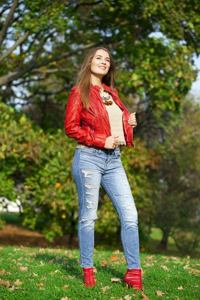 Mujer joven en chaqueta roja de moda y vaqueros azules en el parque de otoño —  Fotos de Stock