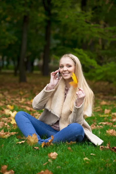 Młody szczęśliwy blond kobieta kontakt telefoniczny w parku jesień — Zdjęcie stockowe