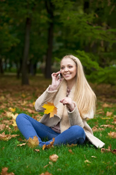 Młody szczęśliwy blond kobieta kontakt telefoniczny w parku jesień — Zdjęcie stockowe