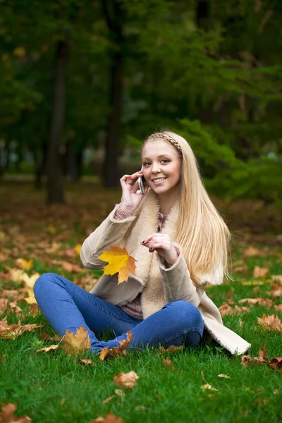 Joven mujer rubia feliz llamando por teléfono en el parque de otoño — Foto de Stock