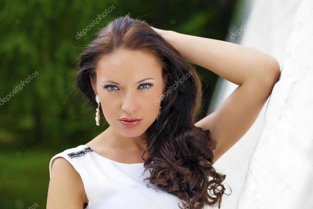 Portrait of beautiful sad girl in white dress leaning on the wal