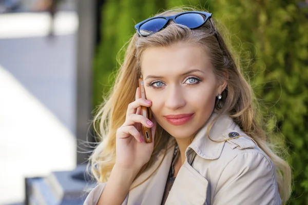 Happy beautiful blonde girl calling by phone in a summer street — Stock Photo, Image