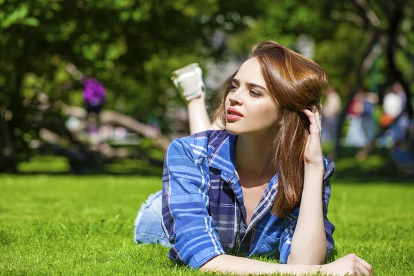 Jonge mooie bruinharige vrouw liggen op een gazon — Stockfoto
