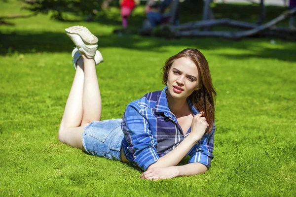 Junge schöne Frau mit braunen Haaren auf dem Rasen liegend — Stockfoto