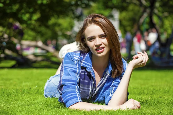 Jonge mooie bruinharige vrouw liggen op een gazon — Stockfoto