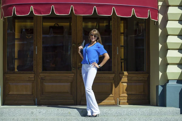 Kvinna i vita byxor och blus poserar på bakgrund av s — Stockfoto