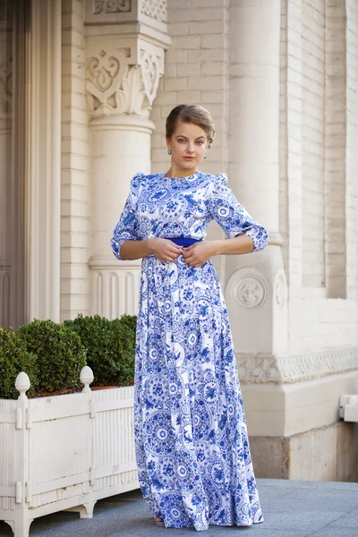 Prachtige blond meisje in blauwe jurk poseren tegen een achtergrond — Stockfoto