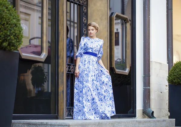 Menina loira bonita em vestido azul posando contra um fundo — Fotografia de Stock