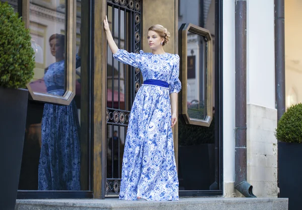 Prachtige blond meisje in blauwe jurk poseren tegen een achtergrond — Stockfoto