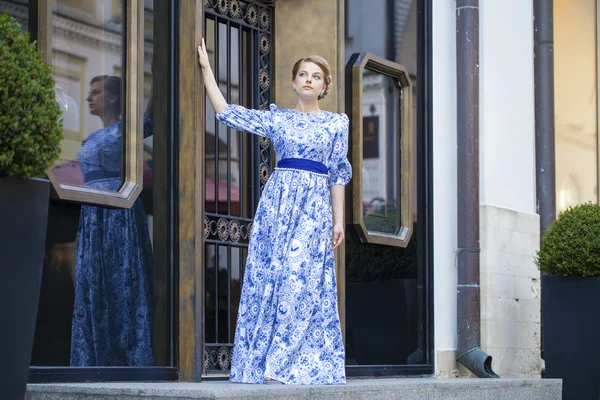 Menina loira bonita em vestido azul posando contra um fundo — Fotografia de Stock