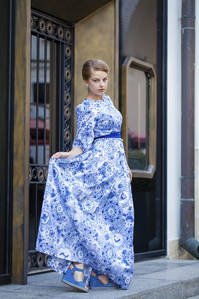 Beautiful blonde girl in blue dress posing against a background — Stock Photo, Image