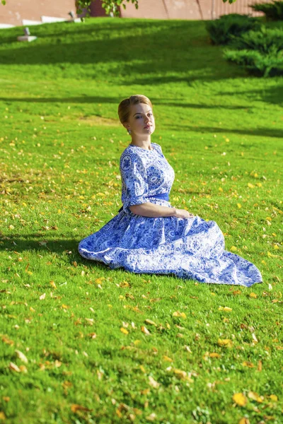 Beautiful blonde girl in blue dress posing against a background — Stock Photo, Image